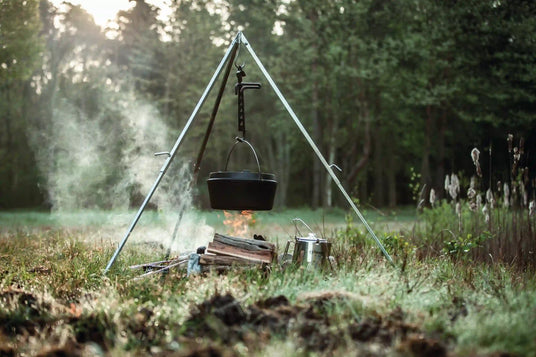 gusseiserner Dutch Oven hängt an einem Dreibein über einem brennenden Lagerfeuer