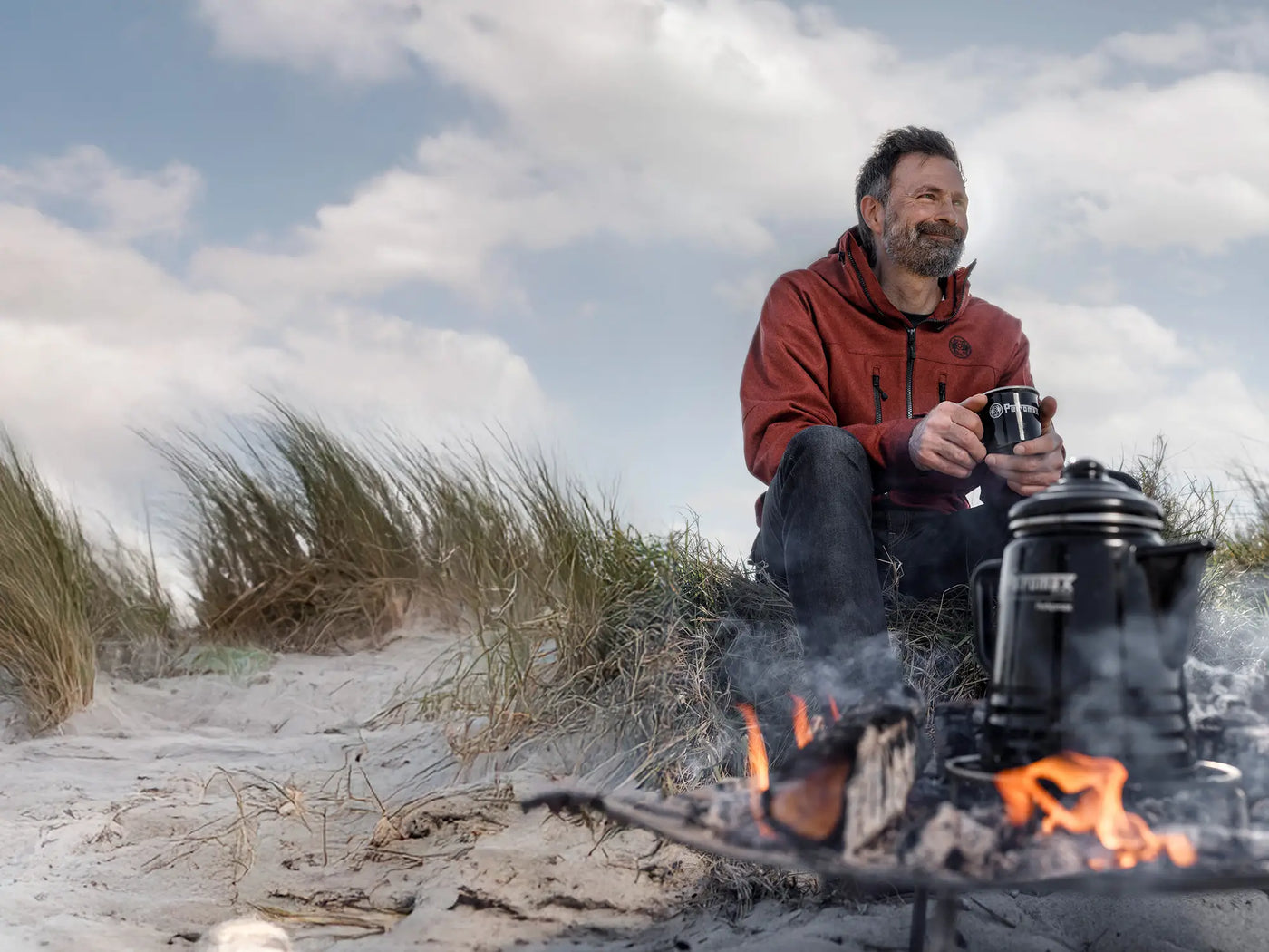 Mann sitzt am Strand mit Petromax Perkolator Kaffee Tag des Kaffees